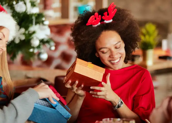 Friends giving and opening Christmas presents next to Christmas tree