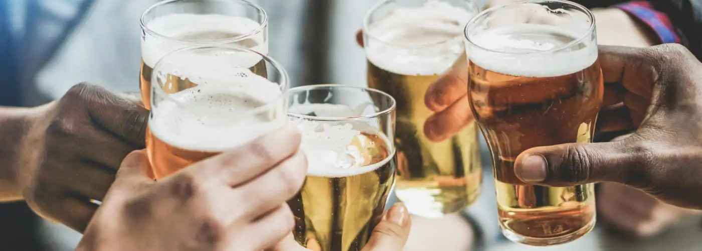 Close up of hands clinking beer glasses in a large group