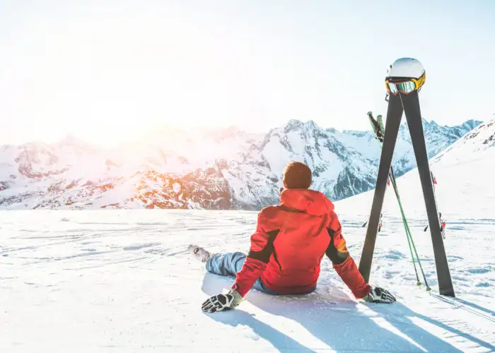 Man sitting next to ski poles looking at mountains