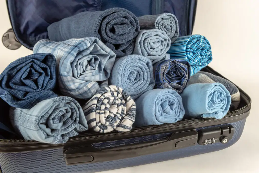 Clothes rolled up in a carry-on suitcase, which is open on an off-white background