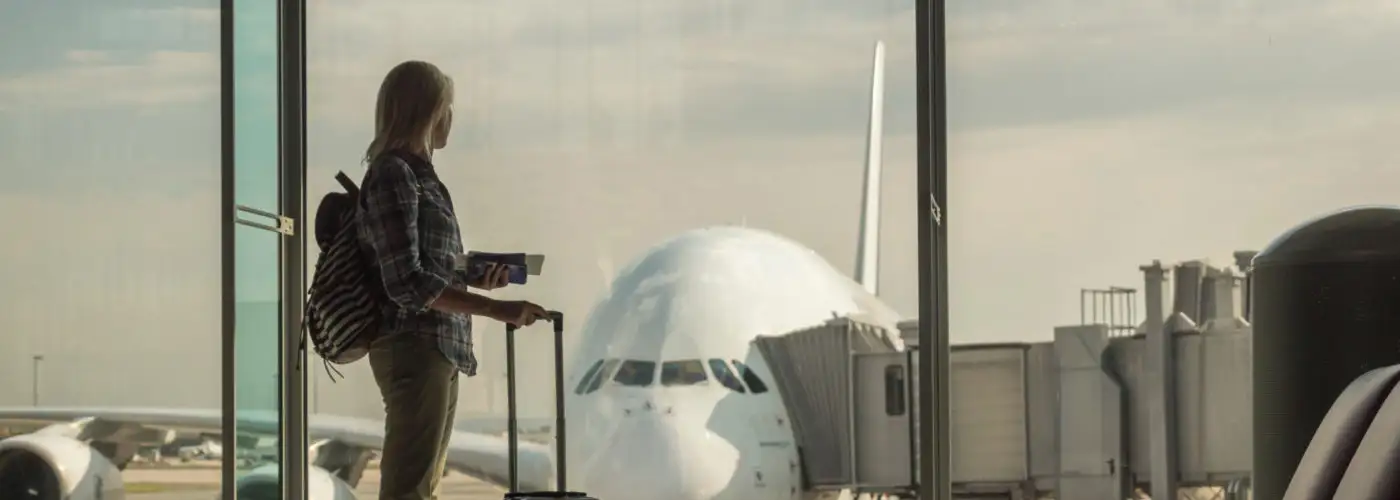 Woman with luggage standing in dark terminal in front of window