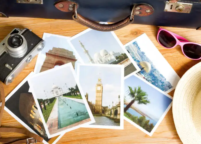 Printed travel photos surrounded by suitcase, sunglasses, and camera