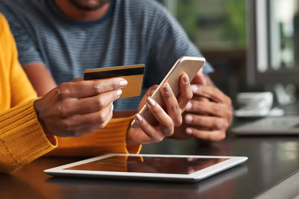 Close up of two people gathered around a tablet and smartphone looking at something on the screens