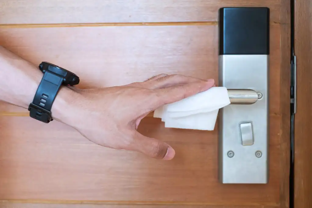 Close up of hand wiping down hotel room door handle with sanitizing wipe