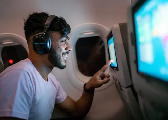 Man wearing bluetooth headphones scrolling through the menu of a seatback screen in an airplane