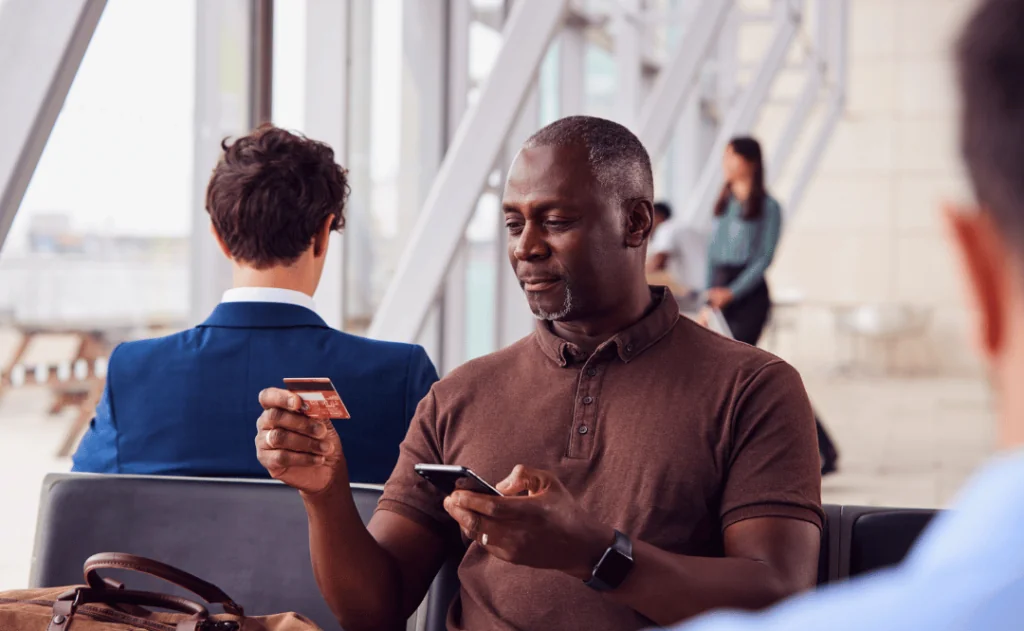 Businessman Sitting In Airport Departure Shopping Online Using Mobile Phone  