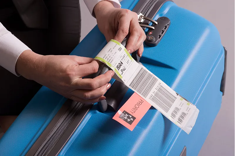 Close up of airline worker attaching a tag to checked luggage