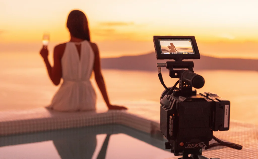 Female travel influencer, recording herself, drinking a glass of wine at sunset next to the pool