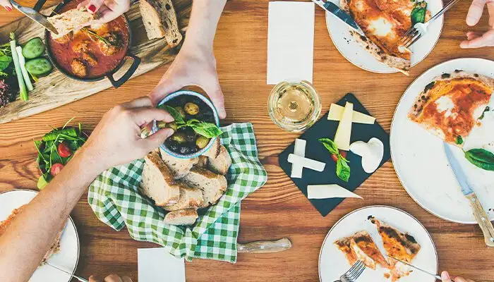 Family or friends summer party or outdoor dinner. Flat-lay of group of people at big table in cafe eating verious food together. Summer gathering or celebration concept