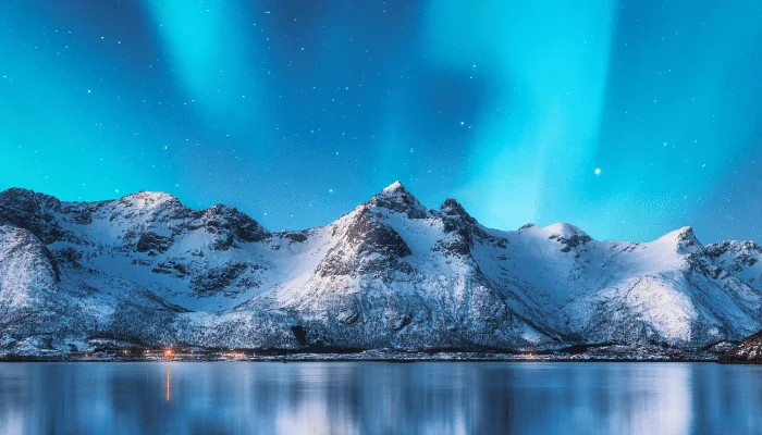 Northern lights and snow covered mountains in Lofoten islands, Norway. Aurora borealis. Starry sky with polar lights and snowy rocks reflected in water.