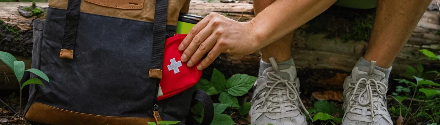 Hiker man crouching in a forest, packing a first aid kit into a backpack, emphasizing preparedness and safety during outdoor adventures