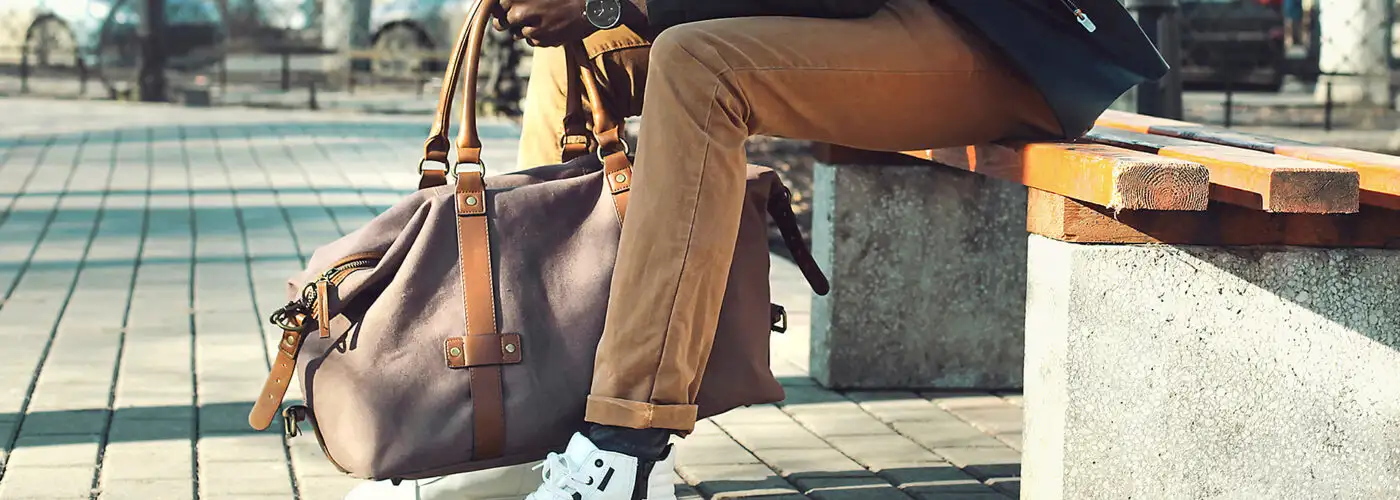 man holding weekender bag sitting bench city