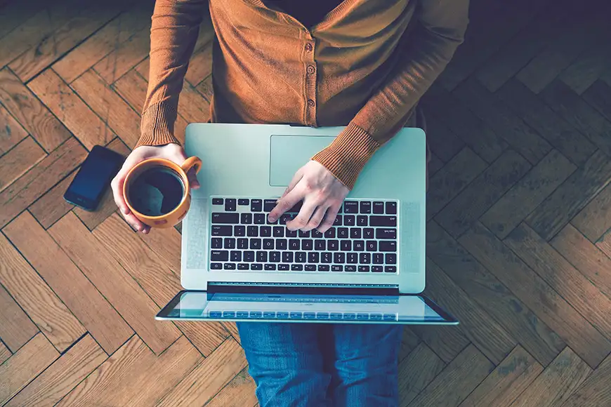 man typing on laptop with a coffee in hand