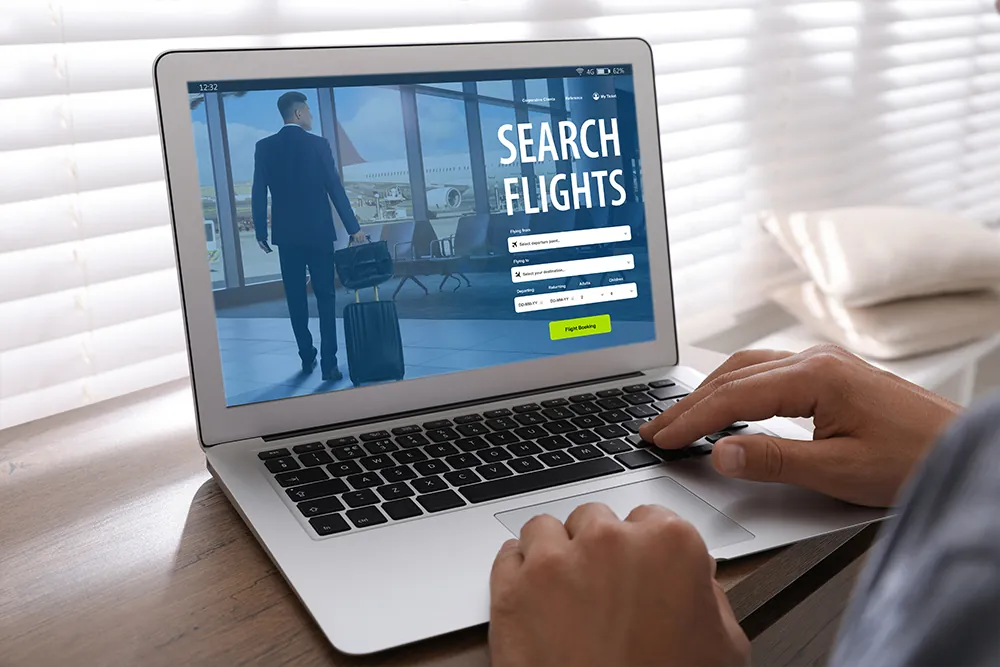 Man using laptop to book flight at wooden table