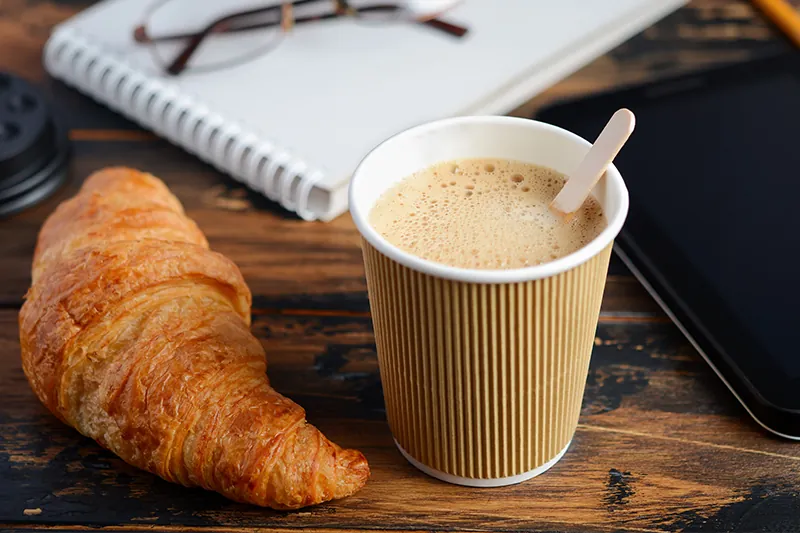 To-go coffee on a table with a croissant and a notebook