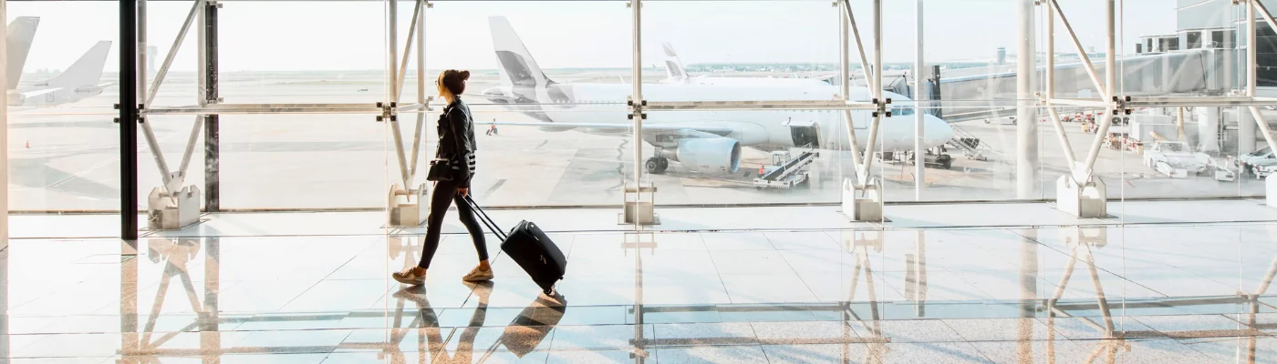 View on the aiport window with woman walking with suitcase at the departure hall of the airport