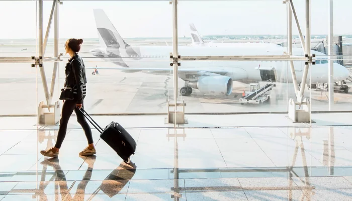 View on the aiport window with woman walking with suitcase at the departure hall of the airport