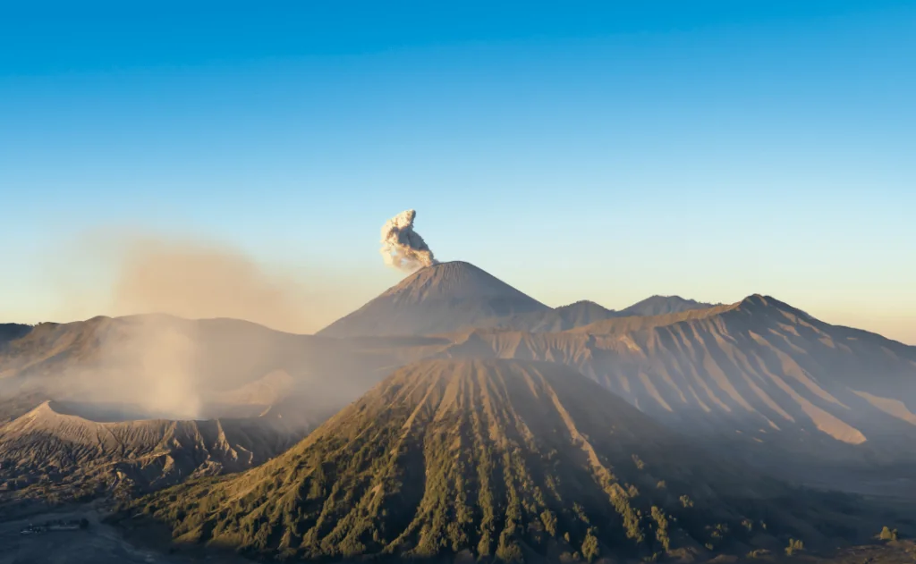 Volcano spewing smoke into sky among natural mountain landscape