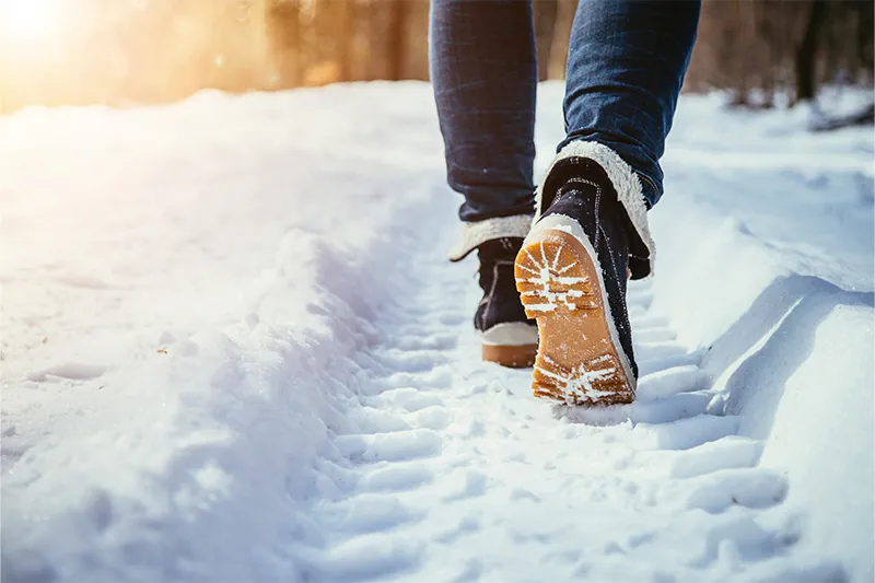 Close up of person wearing winter boots, walking away from the camera in the snow