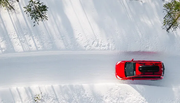 Aerial view of red car driving through snowy forest