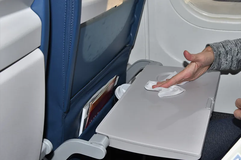 Person wiping down tray table on airplane