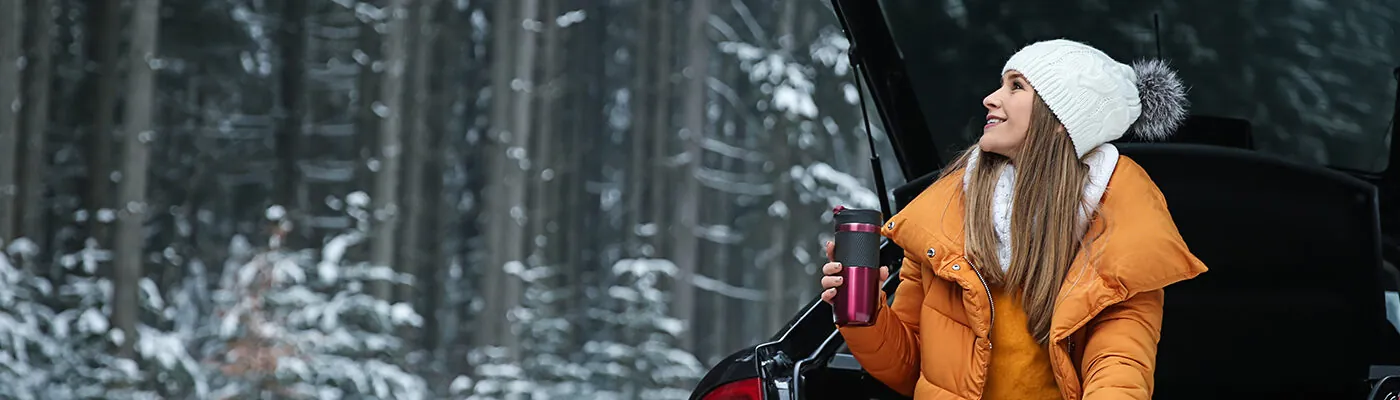 Woman sitting in open trunk of car, drinking coffee in the snow