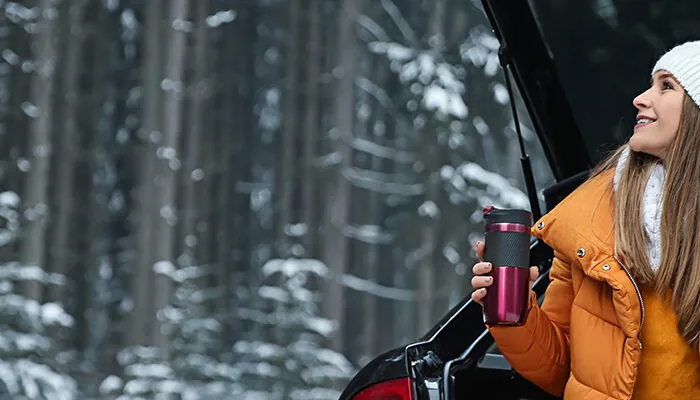 Woman sitting in open trunk of car, drinking coffee in the snow