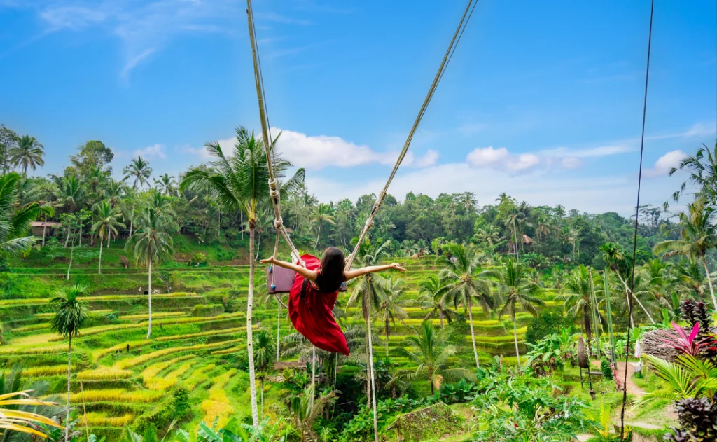 Young female tourist in red dress enjoying the Bali swing at Tegalalang rice terrace in Bali, Indonesia